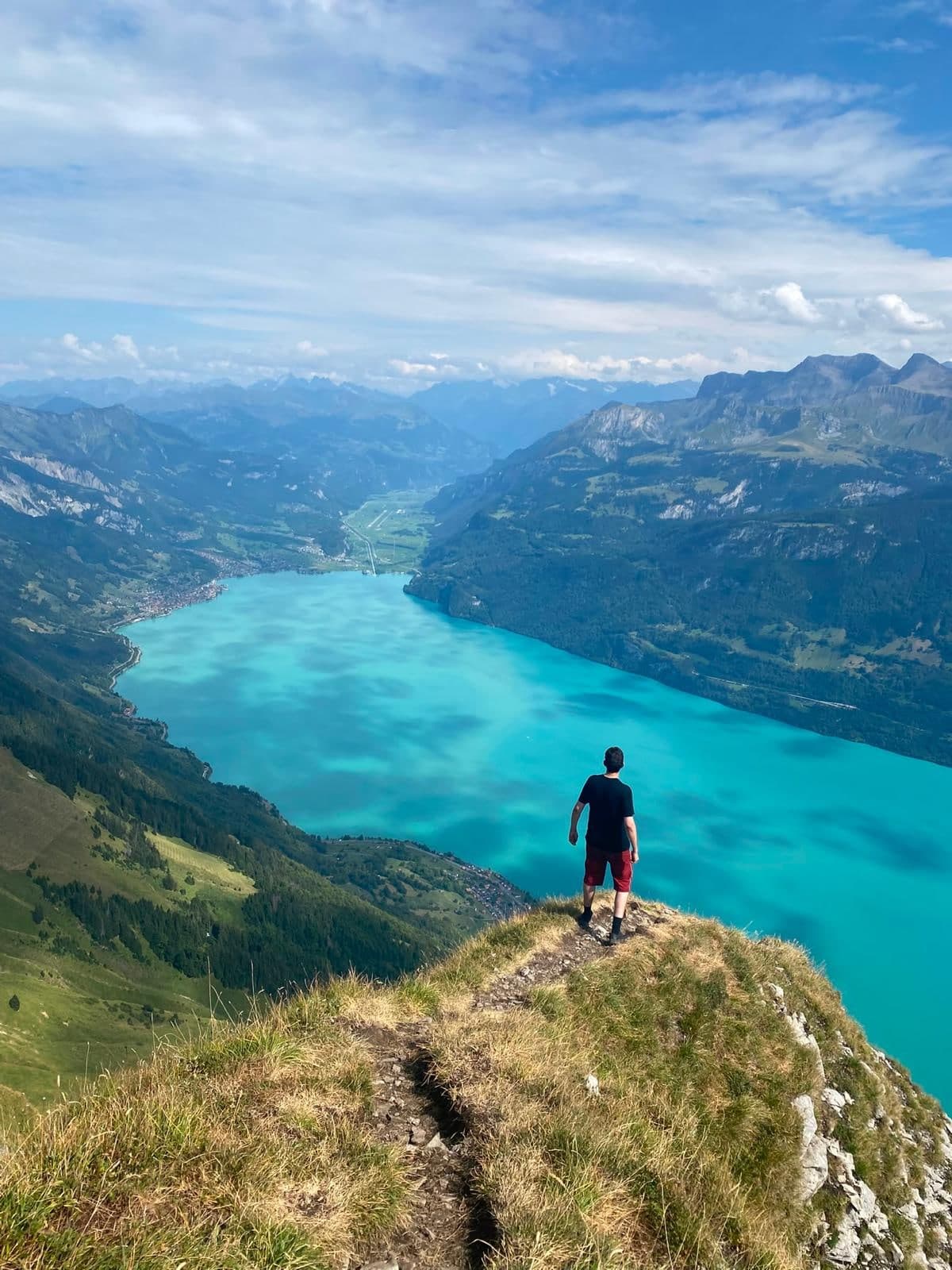 Wanderer steht auf einer Kuppe hoch über dem türkisblauen Brienzersee, umgeben von Bergen