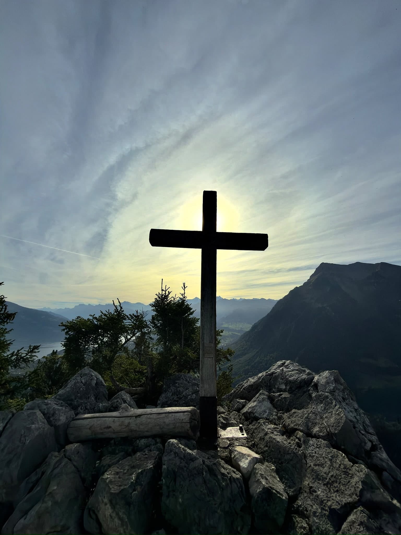 Hölzernes Gipfelkreuz auf Felsen im Gegenlicht