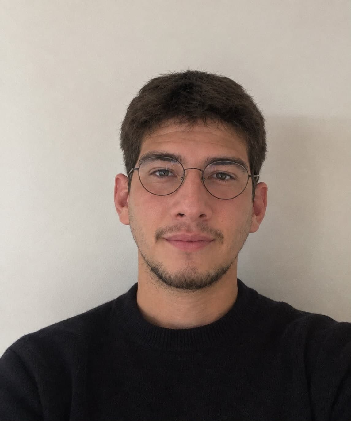 Porträt von Alejandro mit runder Brille und dunklem Pullover
